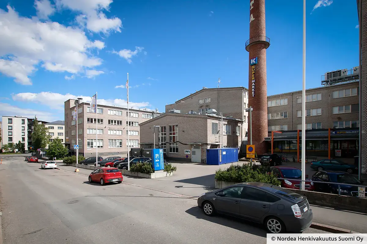 Toimitilakiinteistön Helsingin iviaidankatu 2 itänen osa kuvattuna kadulta. Talon pihalla punainen savupiippu. Kadun varressa pysäköityjä autoja.