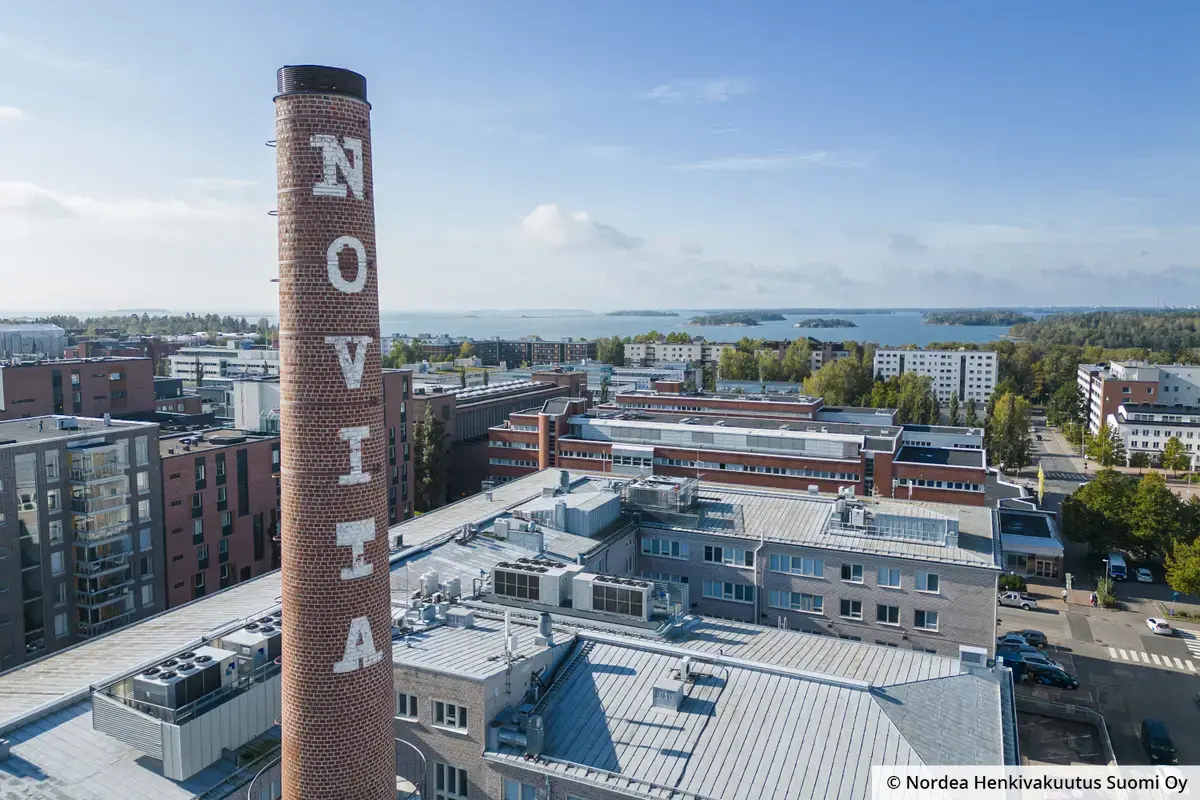 Kiinteistöjen kattoja ja taustalla merimaisema. Etualalla on entisen tuotantolaitoksen piippu, jossa lukee Novita.