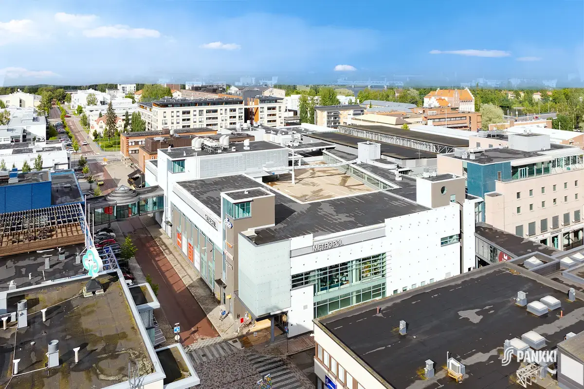 Joensuun Kauppakeskus Metropol ja sen ympäristö ilmasta kuvattuna. Rakennukset ovat matalahkoja noin viiden kerroksen korkuisia. Taustalla on metsää.