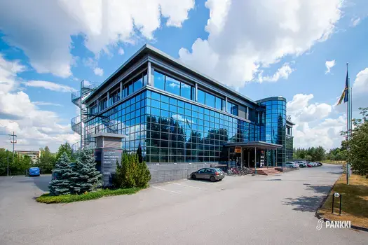 Sinertävin lasielementein verhoiltu toimitilakiinteistö Turku High Tech Centre 2. Talon pihalla on pysäköityjä autoja.