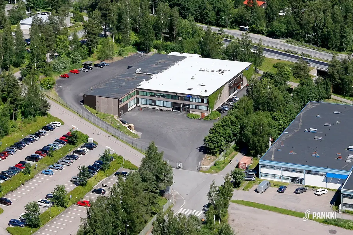 Ilmasta kuvattu matala tasakattoinen toimitilakiinteistö. Rakennuksen oikealla puolella näkyy osa viereisestä rakennuksesta ja etualalla on suuri parkkialue.