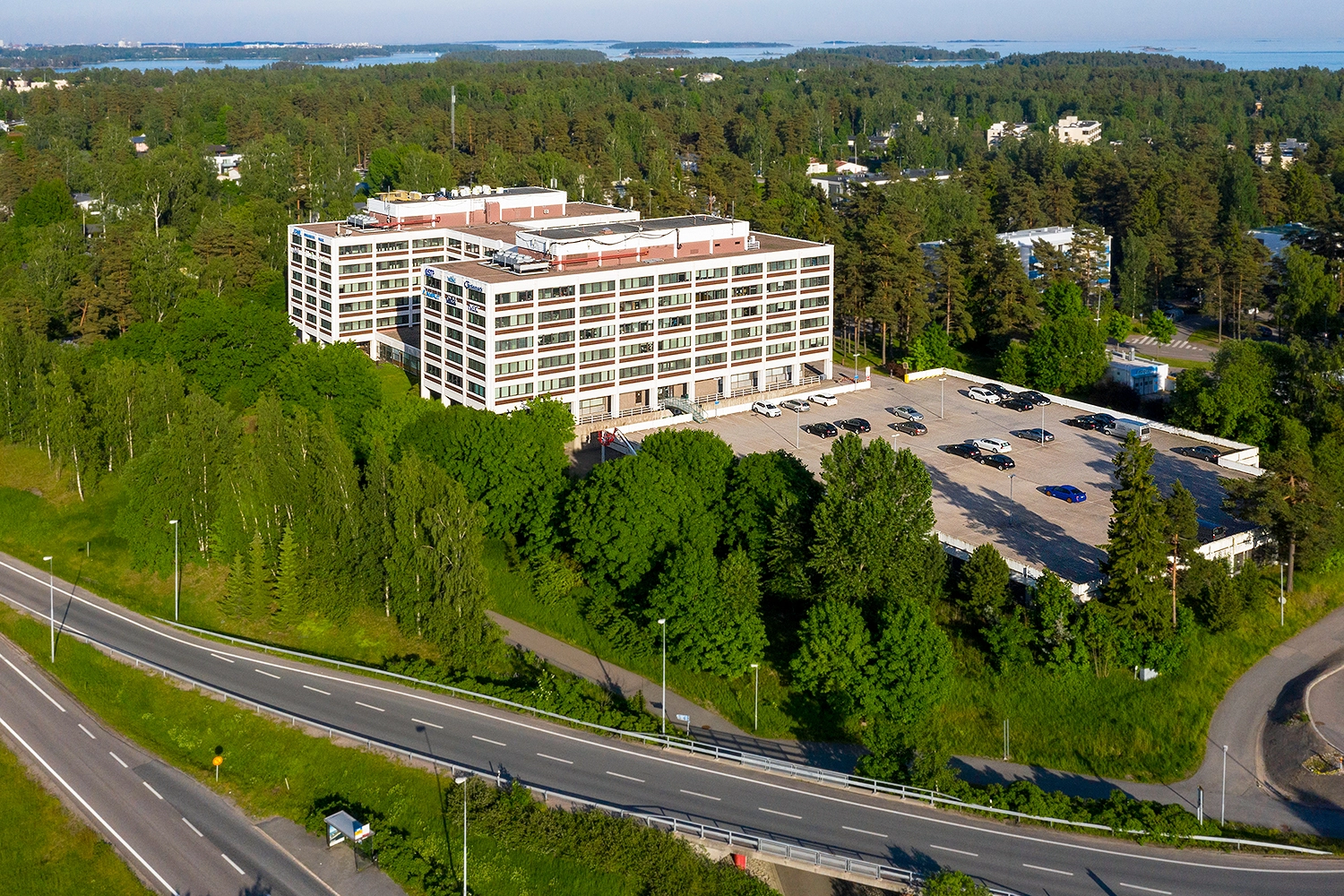Ahti Business Park -toimitilakiinteistu00f6 ilmasta kuvattuna. Vaalea rakennus on keskellu00e4 vehreu00e4u00e4, puistomaista ympu00e4ristu00f6. Rakennuksen edessu00e4 on pysu00e4ku00f6intialue.