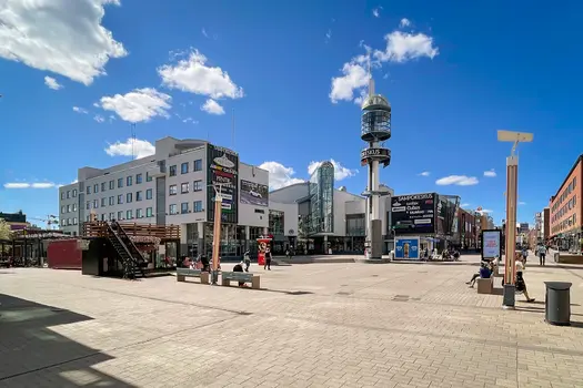 Sampokeskuksen julkisivu. Rakennuksen edessä on torialue, jonka keskellä on korkea torni.