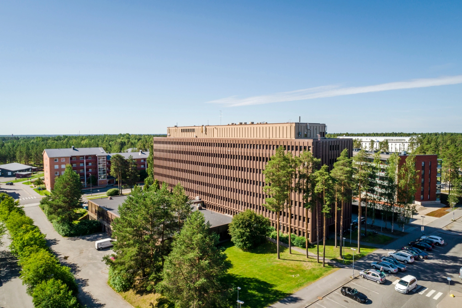 Kiila Business Park ilmasta kuvattuna. Ruskea suuri toimitilakiinteistu00f6 vehreu00e4ssu00e4 ympu00e4ristu00f6ssu00e4.