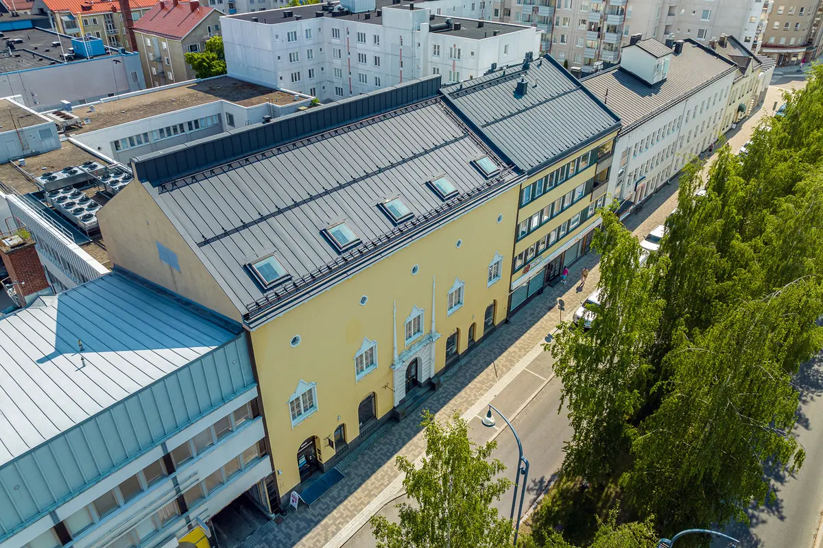 1900-luvun alun keltainen harjakattoinen kerrostalo kesäpäivänä. Talon ympärillä on uudempaa kerrostalokantaa.
