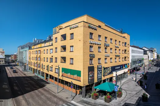 Kauppakortteli Pekuri, toimitilakiinteistön ulkokuva. Monikerroksinen keltainen rakennus, seinillä yrityksien nimikylttejä. 