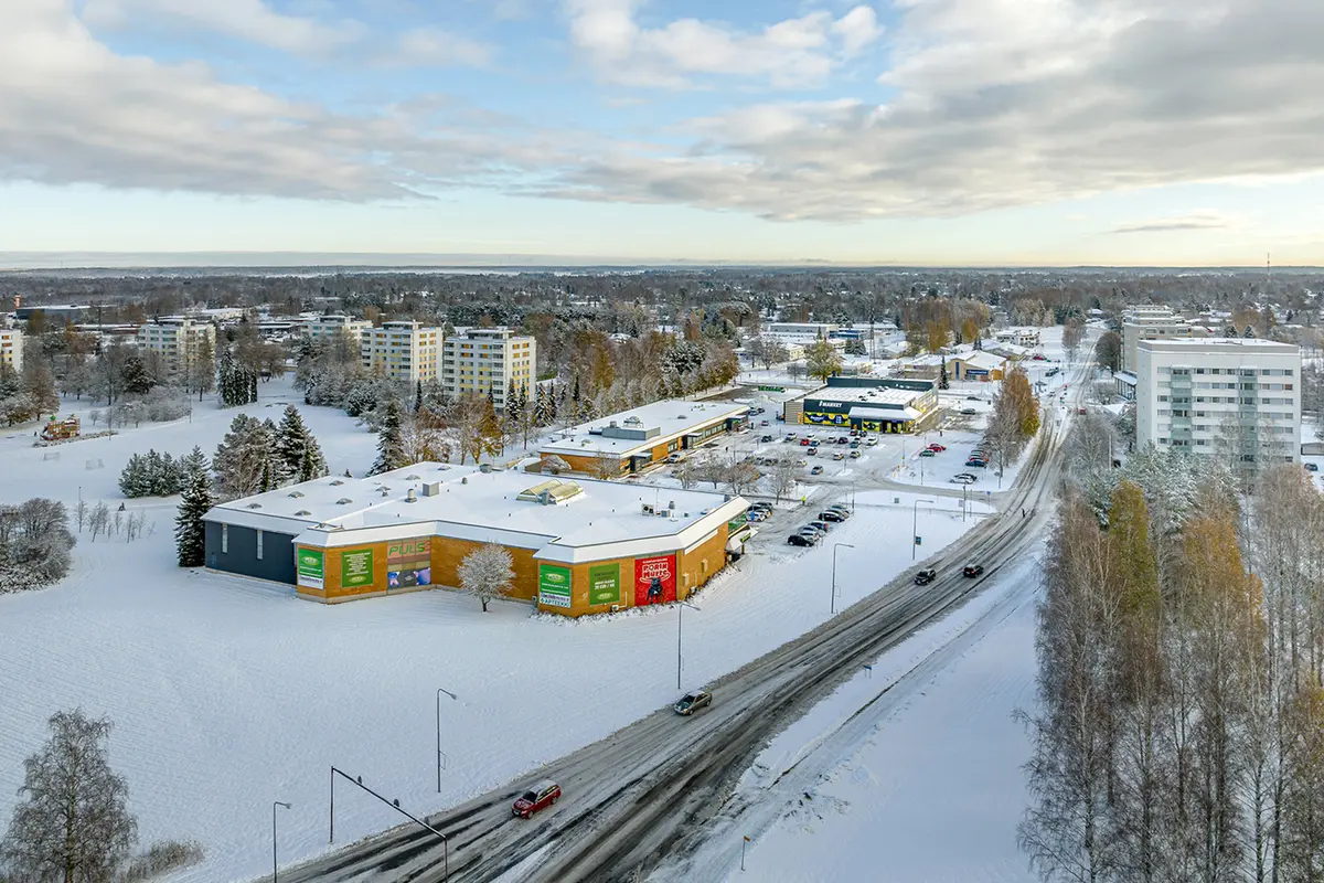 Kolmen liikerakennuksen pihapiiri ilmakuvassa. Keskellä paljon pysäköintitilaa, taaimmaisessa rakennuksessa S-Market.