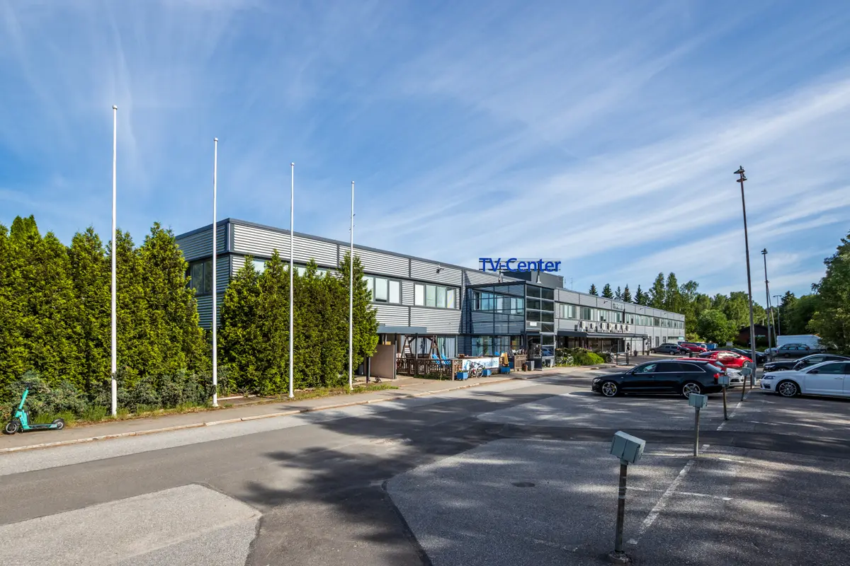 TV-Centerin harmaan sävyinen julkisivu, jonka edessä on pysäköintialue.