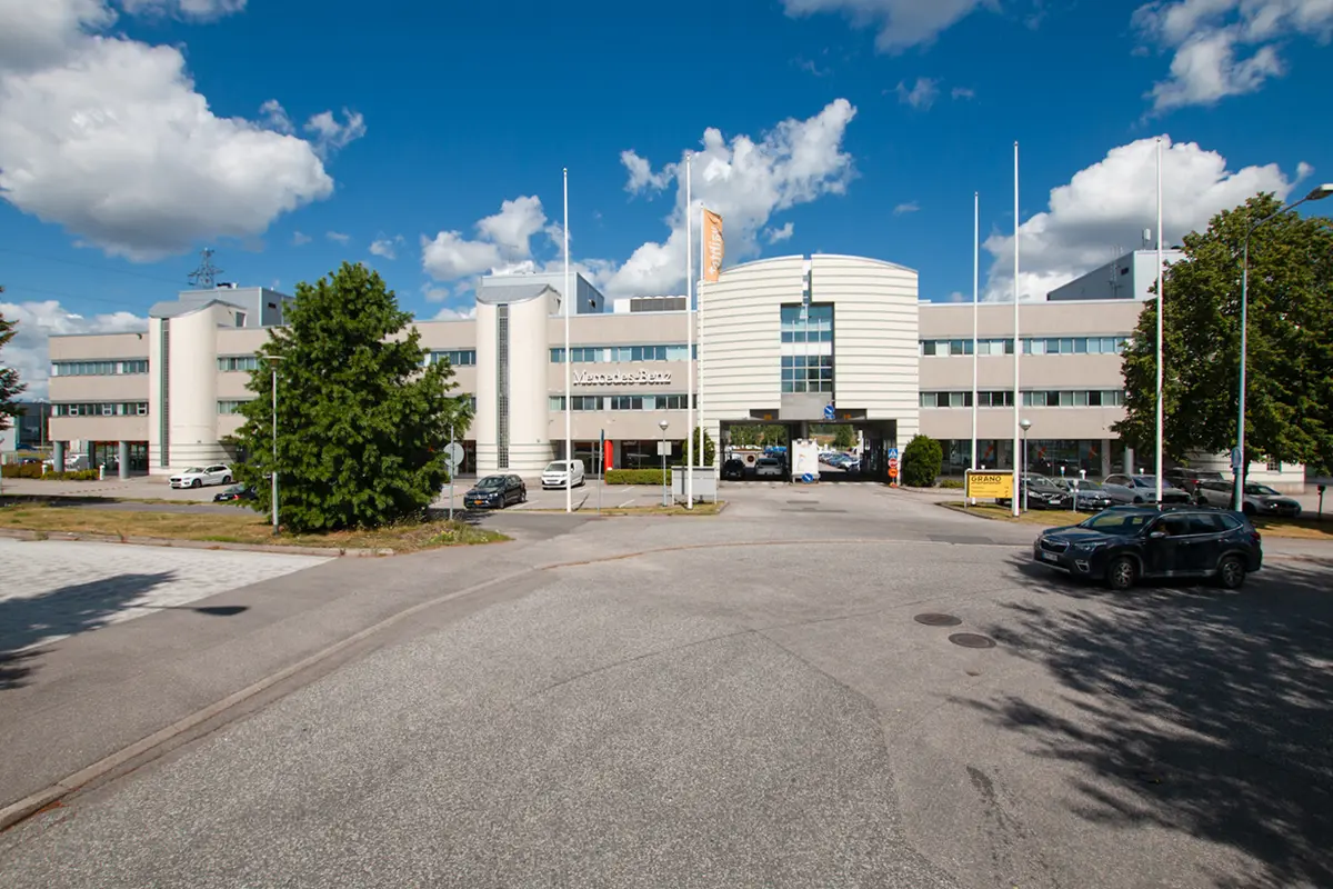 Vaalean kolmekerroksisen toimitilakiinteistön ali pääsee ajamaan autolla. Rakennuksen edessä on lipputankoja.