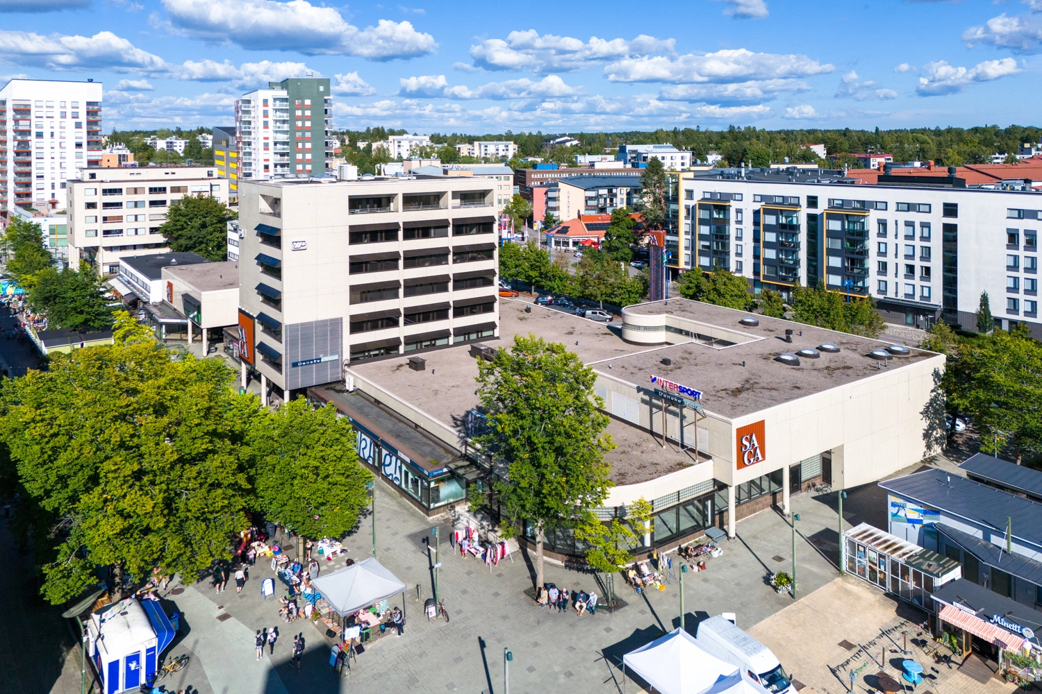 Kauppakeskus Saga -toimitilakiinteistu00f6 ilmasta kuvattuna. Rakennuksen edessu00e4 on tori ja runsaasti ihmisiu00e4 ku00e4velykadulla.
