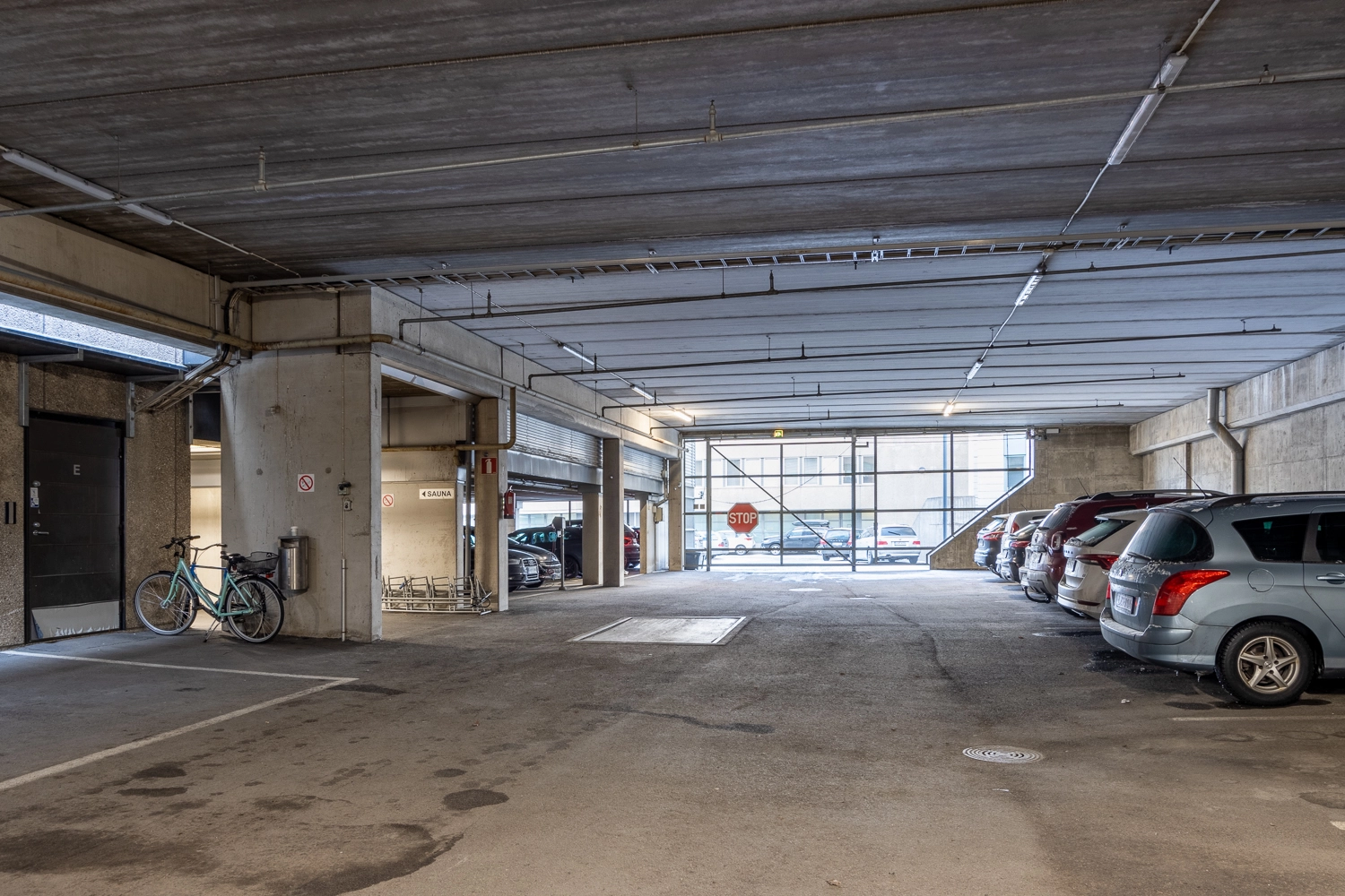 Toimistotalon parkkihalli. Muutamia autoja ja polkupyu00f6ru00e4 pysu00e4ku00f6ityinu00e4.