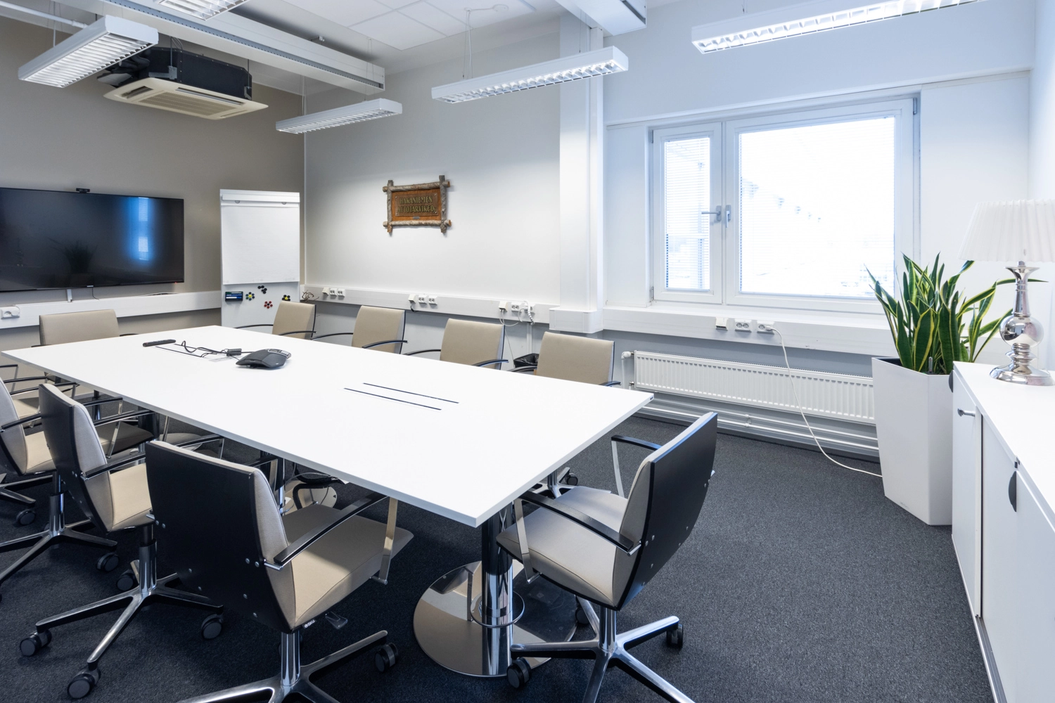 Toimistotalon neuvotteluhuoneen keskellu00e4 on kokouspu00f6ytu00e4 ja 10 tuolia. Seinu00e4lle on ripustettu screen.