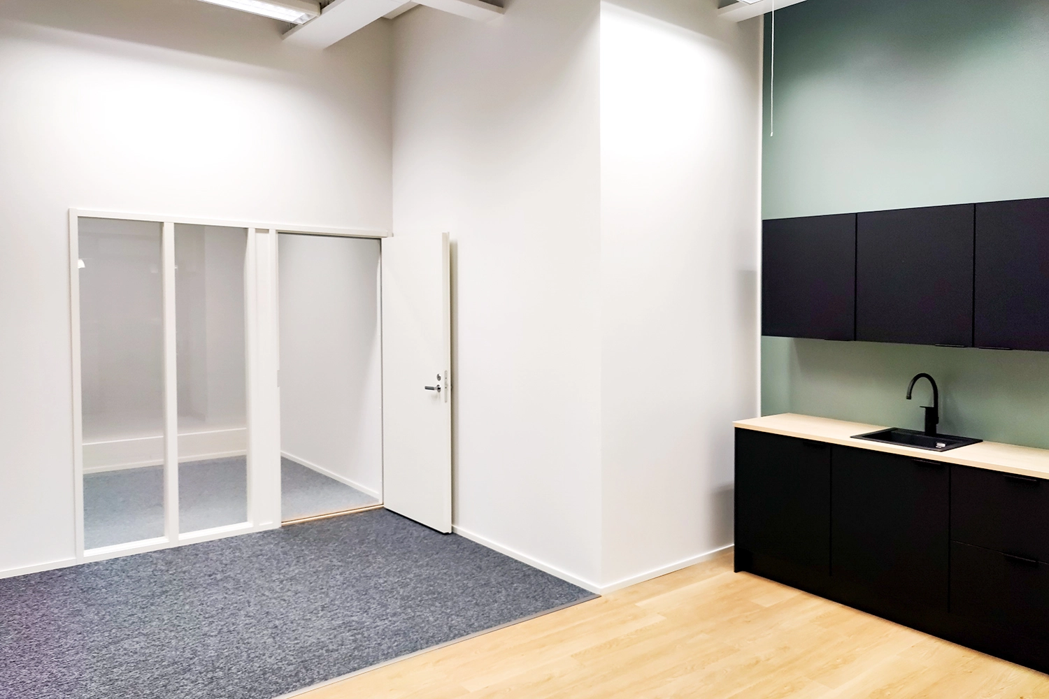 Tampereen Hatanpu00e4u00e4n valtatie 18 toimitilakiinteistu00f6n toimistotila, jossa musta kalusteinen keittiu00f6 ja erillinen pieni tyu00f6huone.