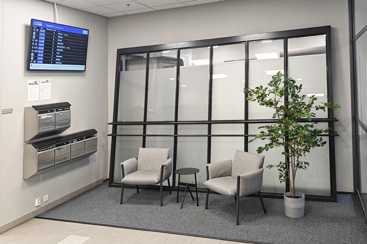 Tampereen Hatanpu00e4u00e4n valtatie 18 toimistorakennuksen odotustila, jossa kaksi tuolia, huonekasvi, ilmoitustaulu ja postilaatikot.
