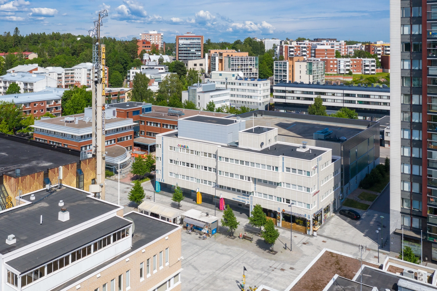 Espoon Tinurinkuja 4, vaalea 4-kerroksinen toimitilakiinteistu00f6 ilmasta kuvattuna. Rakennuksen edessu00e4 on Lu00e4kkitori ja takana nu00e4kyy Leppu00e4vaaran terveysasema seku00e4 asuintaloja.