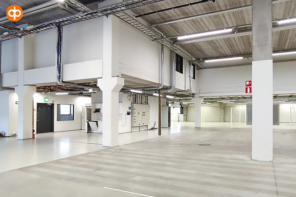 A light-colored warehouse in Vantaa. The space has a couple of supporting pillars, and there are building services on the roof. On the left is a so-called small mezzanine floor with office space.