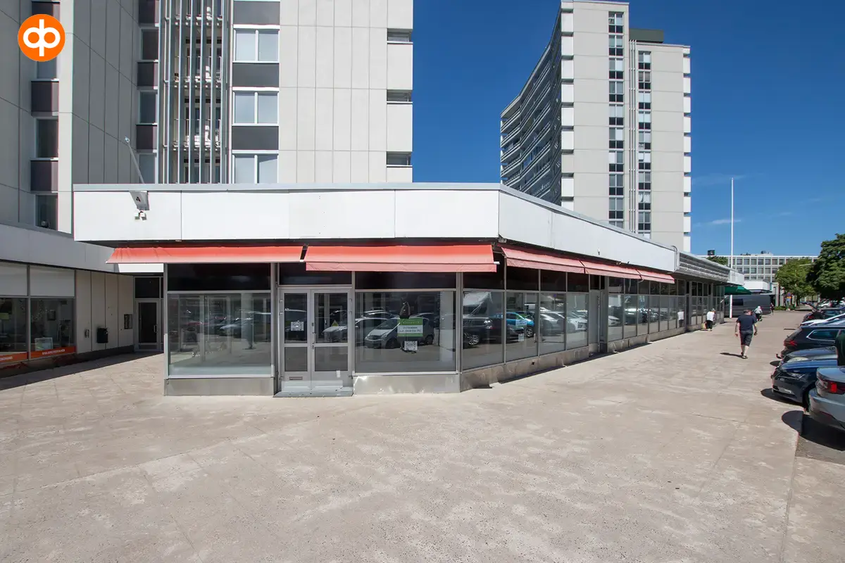 Kuva katutason liiketiloista asuinrakennuksen katutasossa. Liiketilassa on isot ikkunapinnat ja kiinteistön edessä on reilusti parkkipaikkoja.