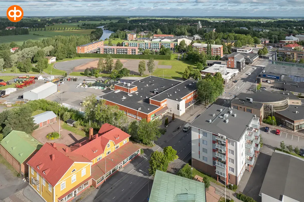 Huittinen Lauttakylänkatu 4, aerial view of the business premises. Flat-roofed red building, surrounded by other buildings, with forest and fields in the background.