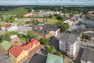 Huittinen Lauttakylänkatu 4, aerial view of the business premises. Flat-roofed red building, surrounded by other buildings, with forest and fields in the background.