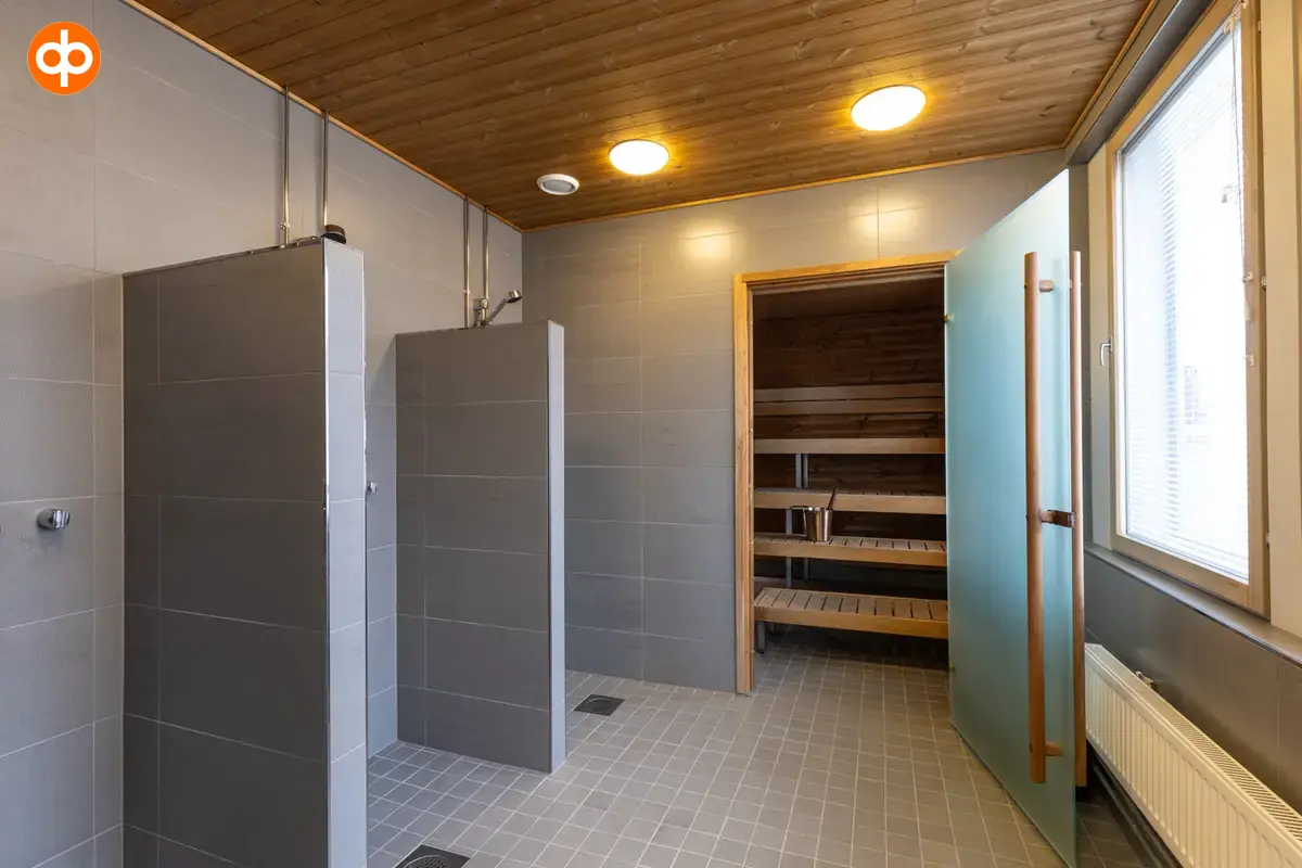 Alberga Business Park – D and E buildings, interior view of the premises. Sauna and shower room in the executive space. Gray tiles on the walls and floor. Two showers on the left with privacy screens.