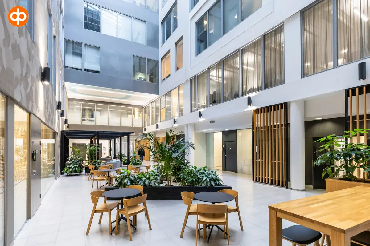 Alberga Business Park, the lounge area of ​​the office building with windows to the office spaces on the upper floors. Table and sofa groups in the lounge. Lots of natural light and greenplants