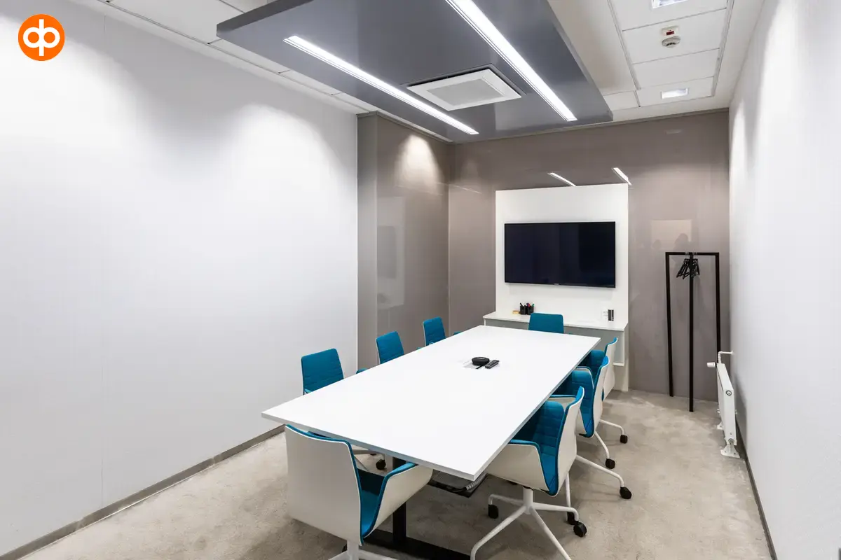 Alberga Business Park, interior view of the office property. A small conference room with a white table in the middle of the room, surrounded by chairs. TV on the back wall. Light carpet in the space.