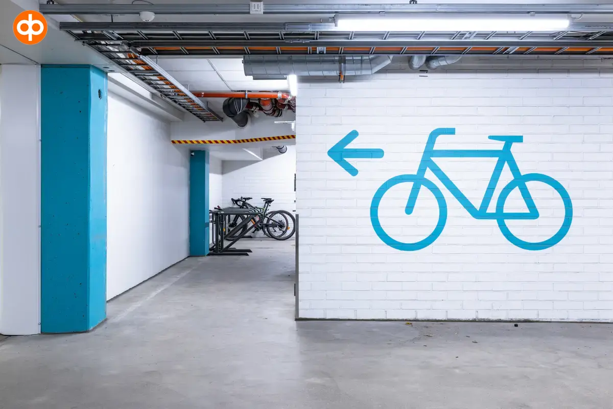 Alberga Business Park – D and E buildings, interior view of the business premises. Bicycle parking in the parking garage, a picture of a blue bicycle on the white wall and an arrow to the left. 