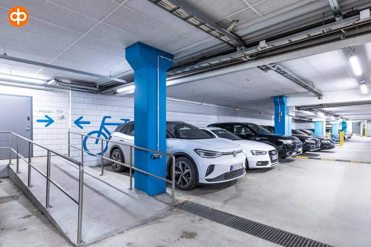 Alberga Business Park – D- ja E-talot, toimitilan parkkihallin sisäkuva. Tilassa autoja pysäköitynä vierekkäin. Autojen välissä siniset betonipylväät. Lattia betonia