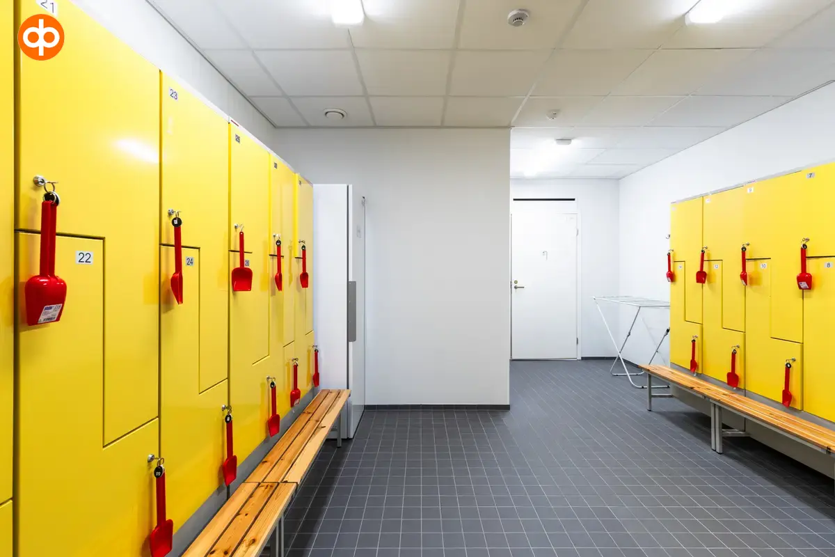 Alberga Business Park – D and E buildings, interior view of the office space. Changing room with yellow lockers on both walls. Children's shovels hanging from the locks as key chains. Grey tiled floor