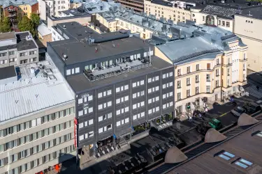 Helsingin Lönnrotinkatu 11, ilmakuva toimitilakiinteistöstä. Tumma monikerroksinen rakennus, jonka vieressä ja takana muita kiinteistöjä. Katutasossa liiketiloja. 