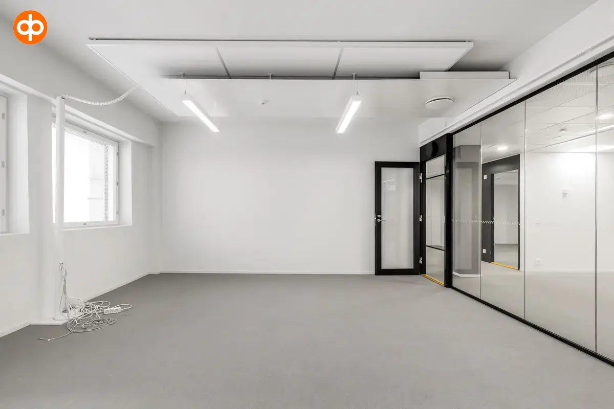 Helsingin Lönnrotinkatu 11, toimitilan sisäkuva. Toimistohuone joka on tyhjä, yksi seinä kokonaan lasia, ovi on musta. 