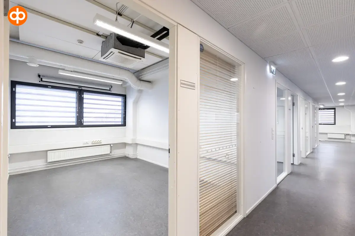 Interior view of the office space on the 2nd floor at Silvastintie 1, Vantaa. The office space has several smaller offices, each with a glass wall to the corridor. The floors are gray and walls white.