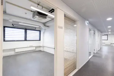 Interior view of the office space on the 2nd floor at Silvastintie 1, Vantaa. The office space has several smaller offices, each with a glass wall to the corridor. The floors are gray and walls white.
