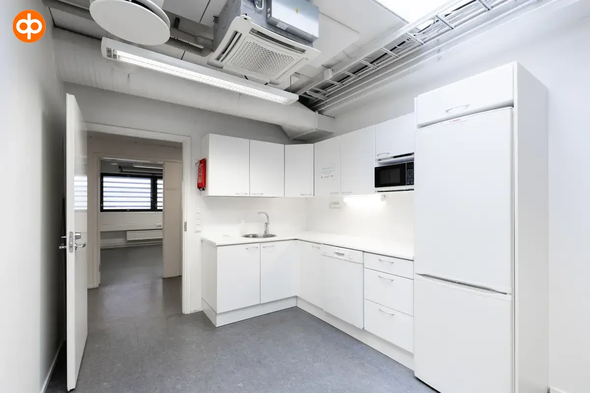 Interior view of the office space on the 2nd floor at Silvastintie 1, Vantaa. A light-colored corner kitchen, next to which is a door to the office corridor. Light gray floors, light walls.
