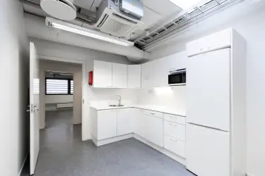 Interior view of the office space on the 2nd floor at Silvastintie 1, Vantaa. A light-colored corner kitchen, next to which is a door to the office corridor. Light gray floors, light walls.