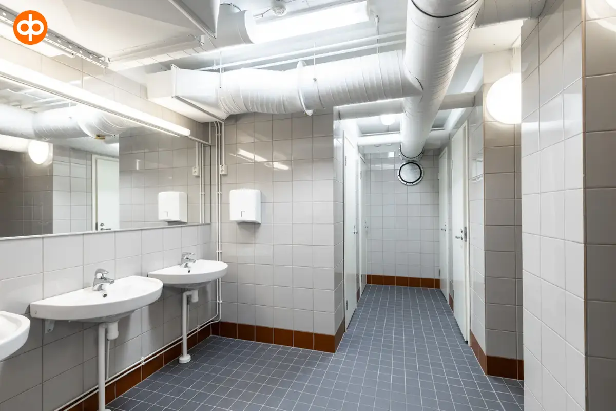 Interior view of the Vantaa Silvastintie 1 office building. Shower room with blue tiled floors and gray wall tiles. Three hand basins on the left, shower cubicles on the right.