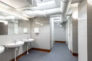Interior view of the Vantaa Silvastintie 1 office building. Shower room with blue tiled floors and gray wall tiles. Three hand basins on the left, shower cubicles on the right.