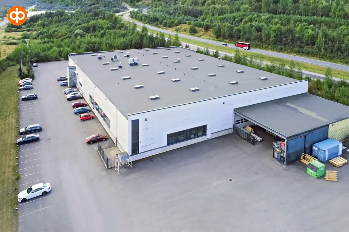 Järvenpää's Tempo 4, exterior view of the office building. White flat-roofed building, asphalted yard with parked cars around the property. A multi-lane road runs behind.