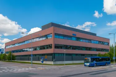 Martinkyläntie 17, toimitilakiinteistön ulkokuva. Kolmekerroksinen rakennus risteyksessä. Rakennus on harmaa ja tiilenoranssi. Oikeassa reunassa bussi.