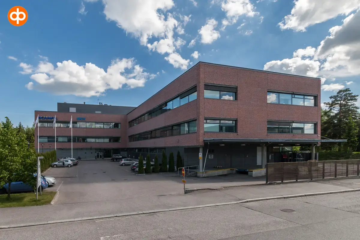 Martinkyläntie 17, toimitilakiinteistön ulkokuva. Kolmekerroksinen rakennus risteyksessä. Rakennus on harmaa ja tiilenoranssi. 