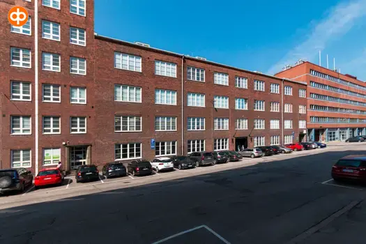 Tekosilkkikutomo toimitilakiinteistön ulkokuva. Punatiilinen monikerroksinen talo, jonka edessä autoja pysäköityneenä. Takana sininen taivas.