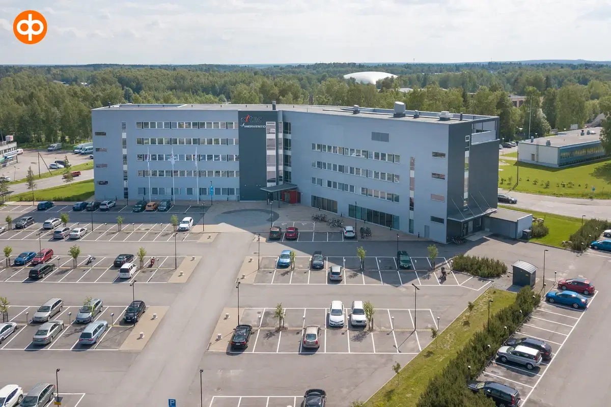 Ilmakuva toimitilakiinteistöstä, jonka taustalla paljon metsää. Edessä suuri pysäköintialue.