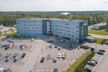Ilmakuva toimitilakiinteistöstä, jonka taustalla paljon metsää. Edessä suuri pysäköintialue.