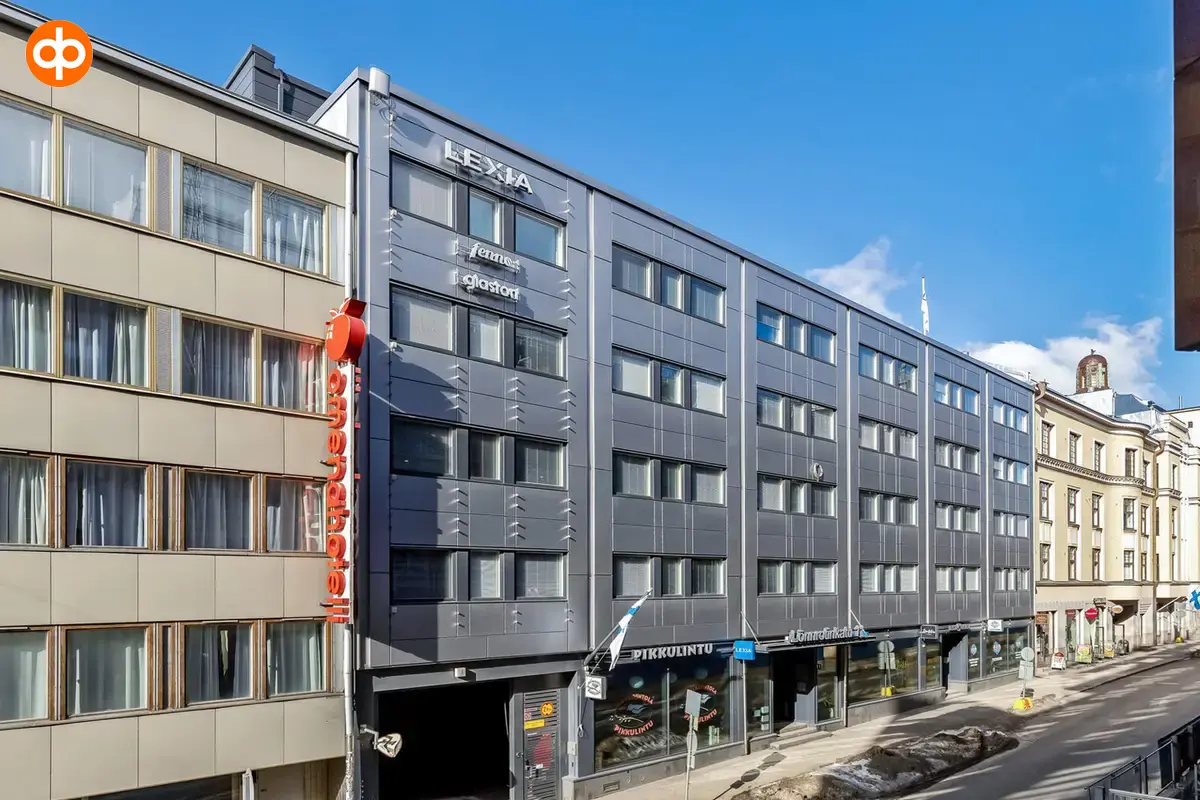 Kiinteistö Lönnrotinkadulla, jonka katutasossa liiketiloja. Rakennuksen edessä kulkee jalkakäytävä sekä autotie.