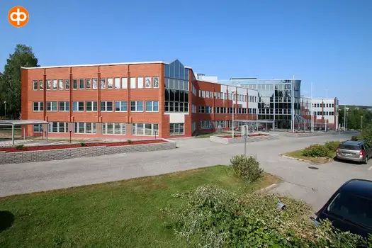 Facade photo of a red brick office building. Parking area in front of the building.